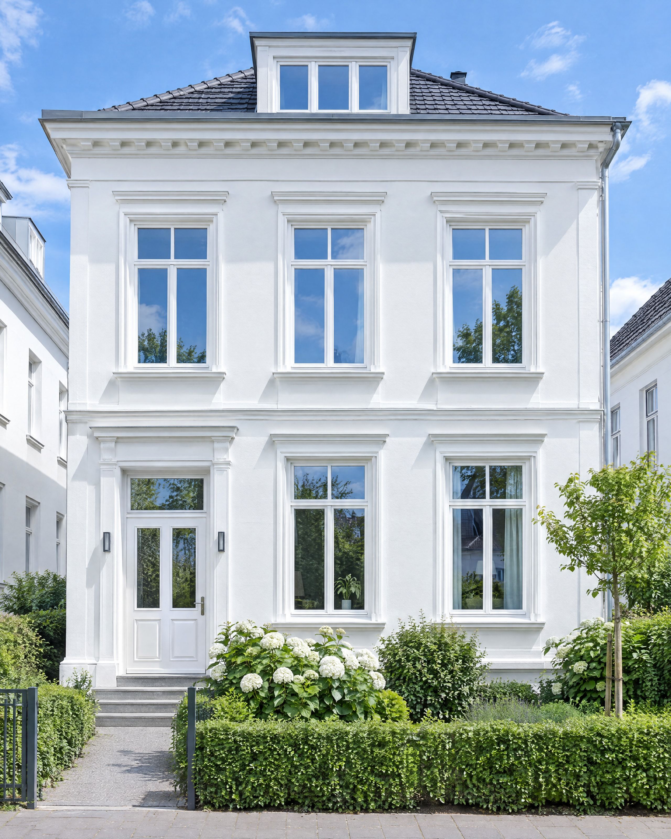 Weißes Stadthaus mit Stuckfassade, hohen weißen Sprossenfenstern und weißer Haustür bei Tageslicht