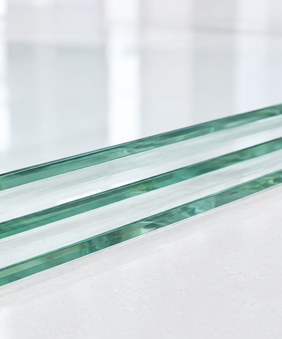 Gestapelte Glasscheiben auf einem hellen Zuschnitttisch, die Kanten schimmern grünlich