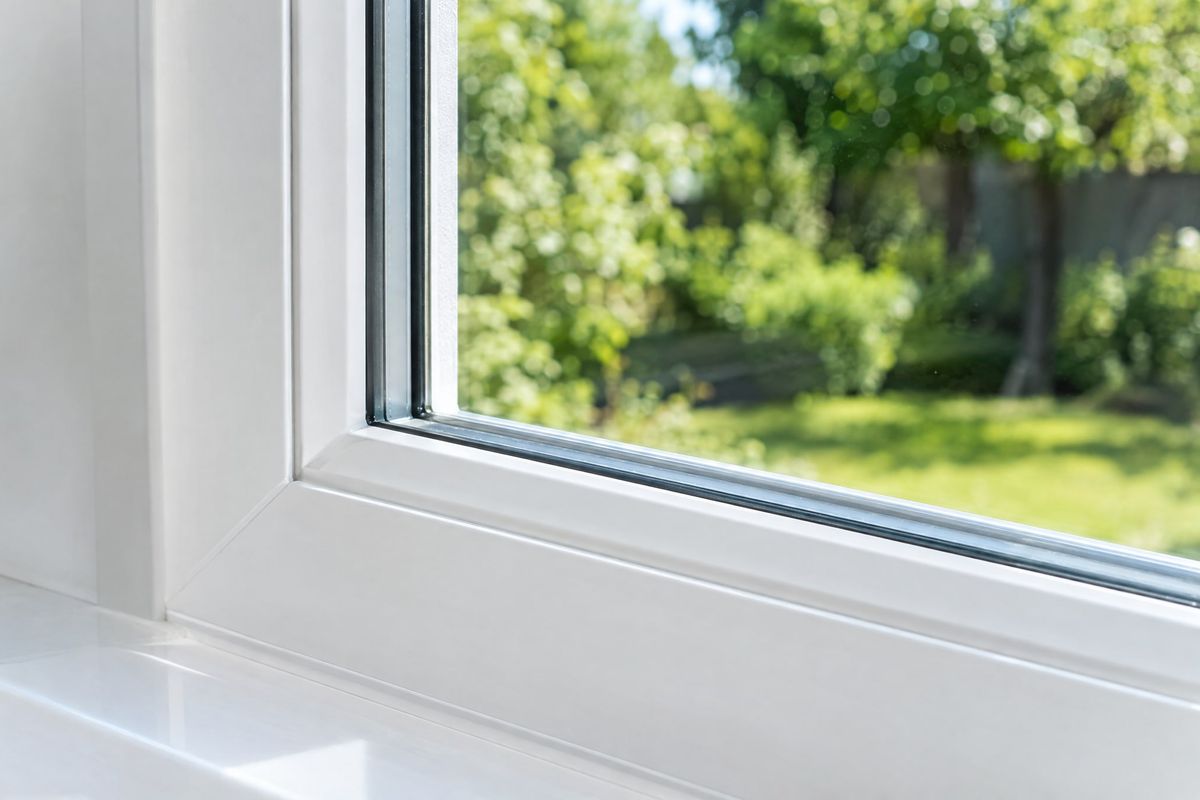 Neu eingesetzte klare Scheibe in einem weißen Fensterrahmen, dahinter unscharf ein grüner Garten